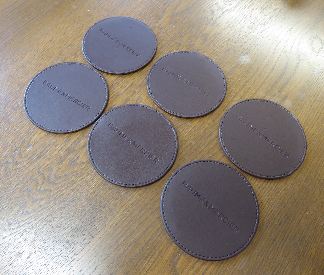 A Set Of Six Baume & Mercier Leather Coasters
